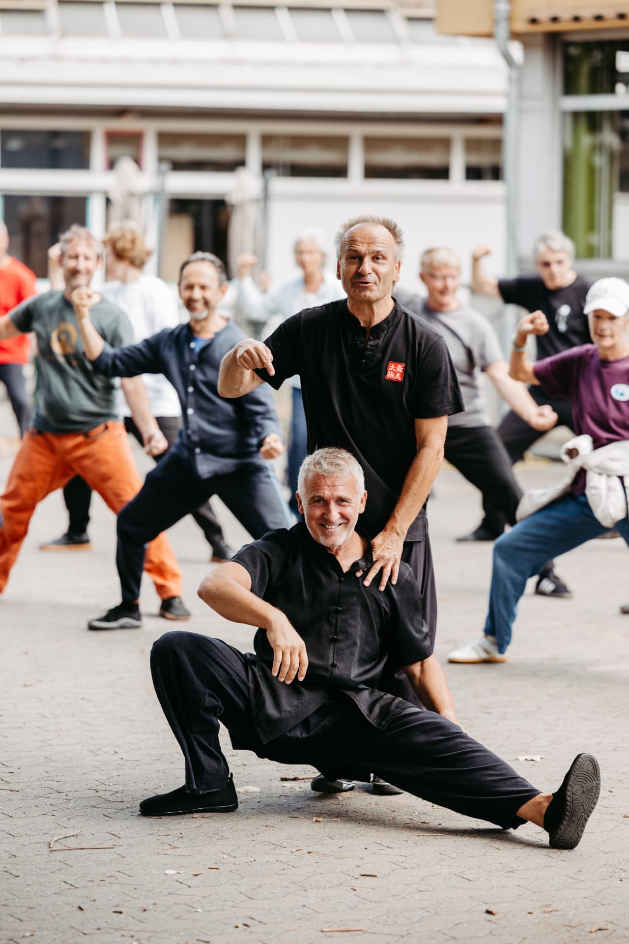 Übende beim gemeinsamen Taijiquan im Freien, im Vordergrund eine tiefe Haltung